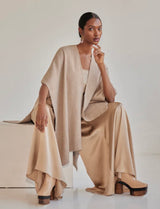 Model wearing a beige alpaca duster over a cream outfit, seated on a light-colored surface.