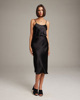 Model wearing a black Bias Midi Skirt in Silk Charmeuse, styled with a simple top and black heels.