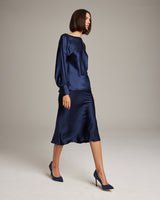 Model wearing a navy silk blouse and bias midi skirt, styled with heels.