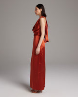 Side view of a model wearing a convertible halter dress in a rich tomato color, showcasing its elegant drape.
