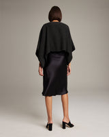 Model wearing a black alpaca crop top over a black satin dress, viewed from the back.