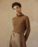 Model wearing a brown ribbed cropped sweater with a high neck and a satin skirt