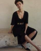 Model wearing a black dress with a silver-plated belt, sitting on a stone surface.