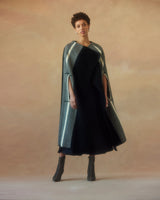 Model wearing a Lineas Cloak with a black dress and boots against a soft background