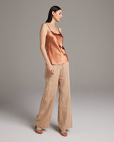 Model wearing a terracotta silk tank top with spaghetti straps and beige pants
