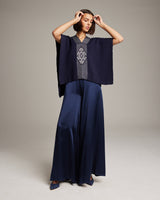 Model wearing a navy poncho with a geometric design and wide-leg pants.