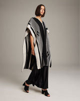 Model wearing the Manta Comunidad poncho in black and ivory, showcasing its design.