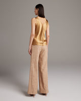 Model wearing a gold silk raw edge tank top and beige palazzo pants from the back