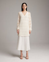 Model wearing a loose knit linen sweater in ivory, paired with a white skirt.
