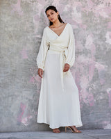 Model wearing a cream peasant blouse with puff sleeves and a matching skirt against a textured background.