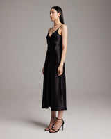 Model wearing a black V-neck slip dress with spaghetti straps, standing sideways.