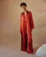 Model wearing a silk Featherlight Wrap Blouse in rust color, standing against a soft background.