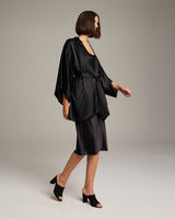 Model wearing a black silk kimono with a matching belt, styled with a skirt and heels.