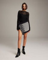 Model wearing a black top and a diamond patterned Diamante Mini Wrap Skirt with fringe.