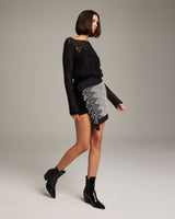 Model wearing a black sweater and a patterned Diamante Mini Wrap Skirt with fringe.
