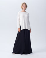 Model wearing a white Cotton Flammé Relaxed Sweater with a boat neckline and side slits, paired with black palazzo pants.