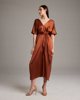 Model wearing a rust kaftan dress with a tie waist and heels