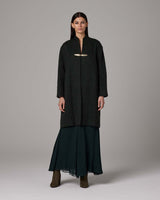 Model wearing a handwoven alpaca Lineas coat in forest color, featuring a sterling silver brooch.