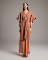 Model wearing a shimmering copper kaftan with a belt, standing against a neutral background.