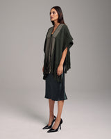 Model wearing a green Lineas Fringe Manta with fringes, styled with a dress and heels.