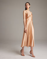 Model wearing a peach V-neck slip dress with spaghetti straps