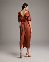 Back view of a model wearing a rust-colored kaftan dress with a deep V-neck and a tied waist.