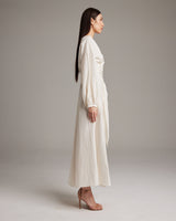 Side view of a model wearing a white Peasant Blouse Dress with long sleeves and a wrap silhouette.