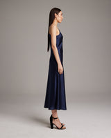 Model wearing a navy V-neck slip dress with spaghetti straps, side view