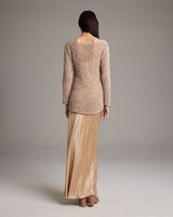Back view of a woman wearing a shimmering loose knit long sweater with a satin skirt