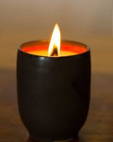 A lit candle in a dark ceramic vessel with a red interior