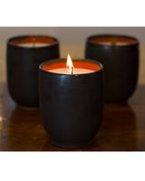 Three hand-poured ceramic candles with a lit wick, featuring a red interior.