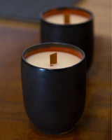 Two hand-poured ceramic candles in black vessels with wooden wicks