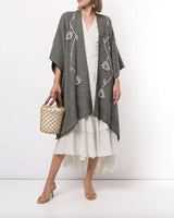 Model wearing a grey Copihue Duster in Baby Alpaca with geometric patterns, holding a woven bag.