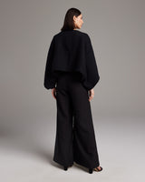 Model wearing a black hand-loomed Jungle Bolero from the back, paired with wide trousers.
