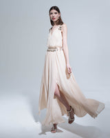 Model wearing a flowing cream dress with a disc jewelry belt, showcasing the outfit's elegance.