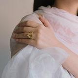 A hand wearing a Millapani Signet Diamond Ring, featuring a gold band and intricate design.