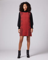 Model wearing a sleeveless brick-colored dress with a black long-sleeve top