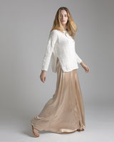Model wearing a white relaxed sweater with a boat neckline and side slits, paired with a flowing beige skirt.