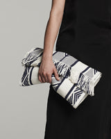 Model holding oversized fringe clutch in navy and ivory with Mapuche symbols