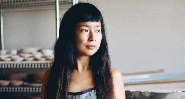 Re Jin Lee standing in a studio with pottery in the background