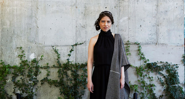 Natalia Oberti Noguera standing against a textured wall with greenery, wearing a black outfit and shawl.