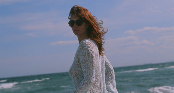 Adele Jacques standing on a beach with sunglasses and wind-blown hair