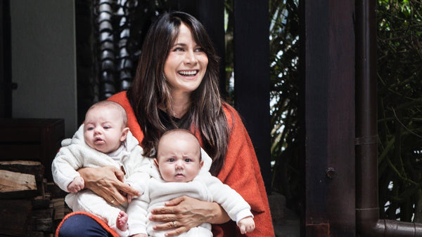 Michelle Arévalo-Carpenter smiling while holding two babies in white outfits