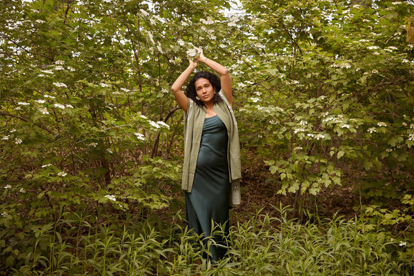 Suanny Upegui standing in a green setting with flowers, wearing a green dress and shawl