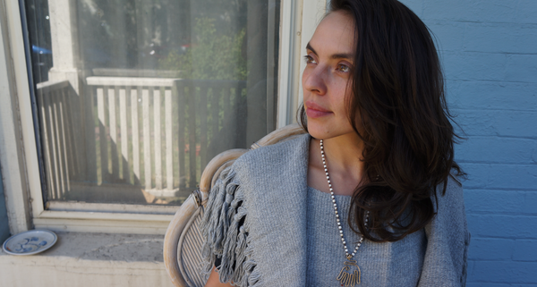 Eutimia Cruz Montoya wearing a gray shawl and necklace, seated by a window